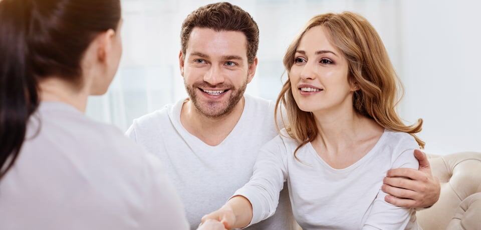 Pareja sonriente estrechando manos con persona enfrente.
